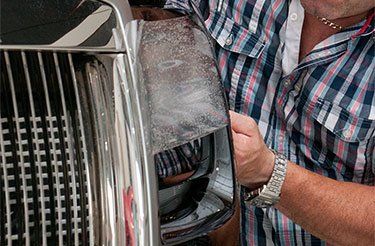 Un homme en chemise à carreaux travaille sur l'avant d'une voiture.