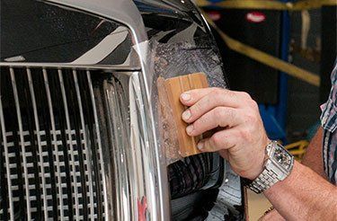 Un homme enveloppe une voiture avec une brosse en bois.