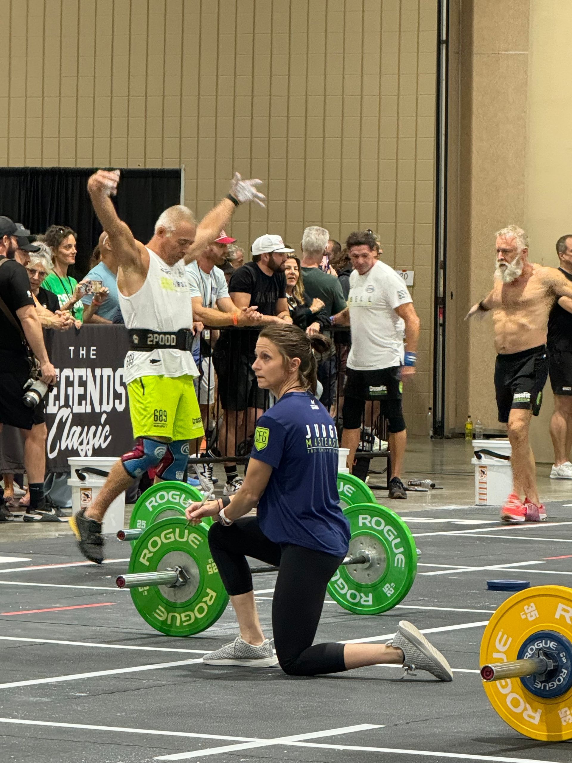A woman is kneeling down next to a man lifting weights in a gym.