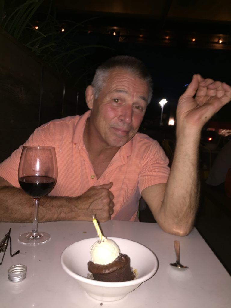 A man is sitting at a table with a glass of wine and a bowl of dessert.