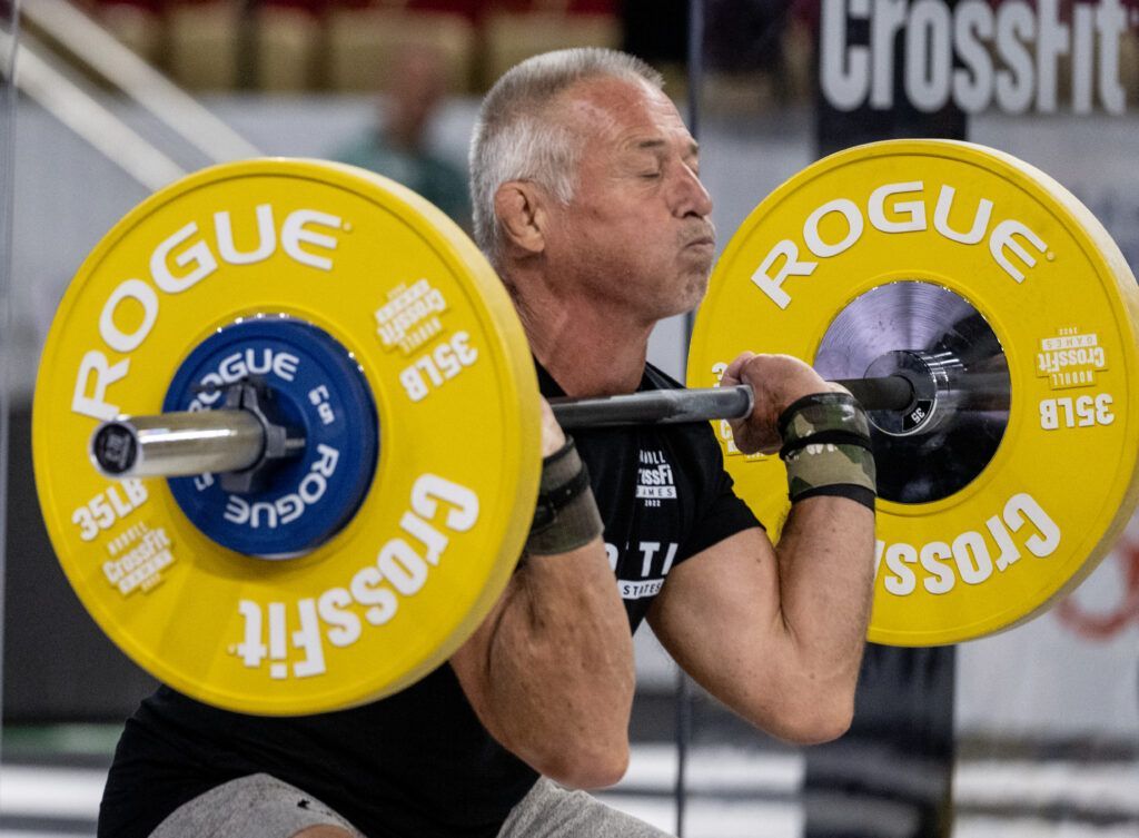 A man is squatting with a barbell with rogue plates on it.