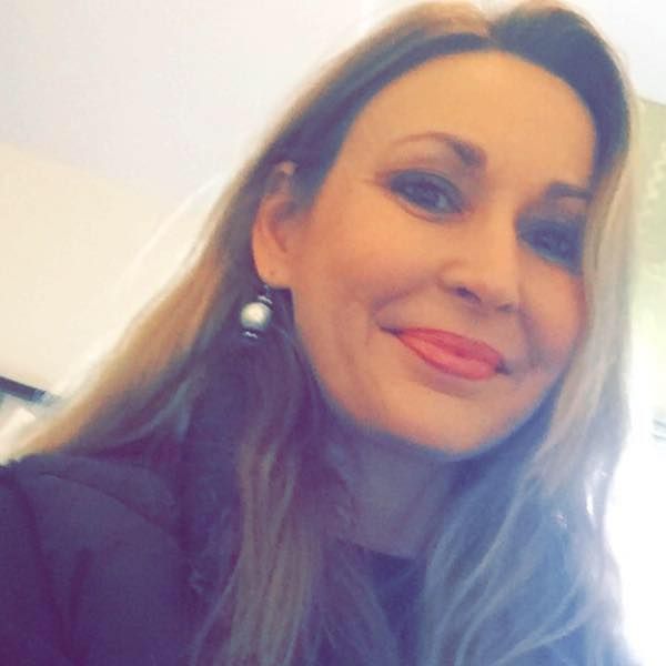 A woman wearing a black shirt and earrings is smiling for the camera.