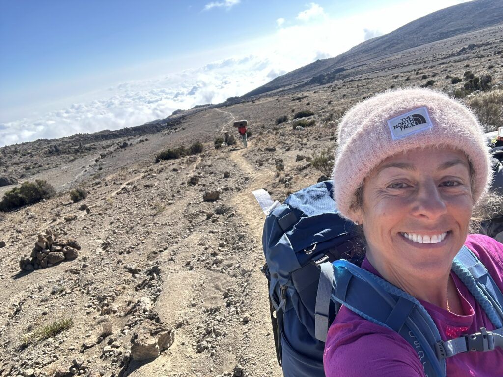 A woman wearing a pink hat and a backpack is hiking on a dirt path.