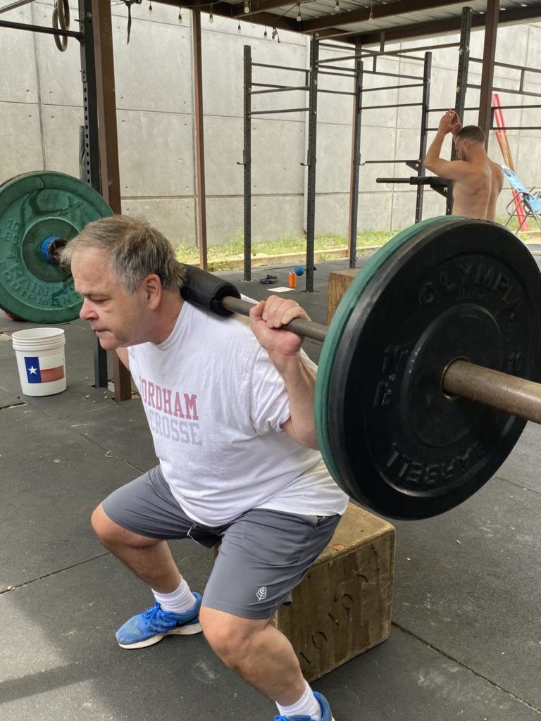 A man is squatting down with a barbell on his back.