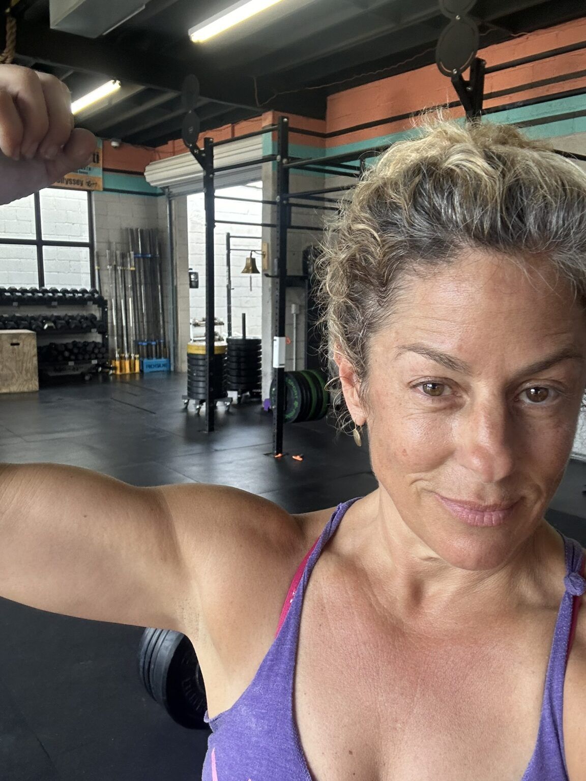 A woman in a purple tank top is flexing her muscles in a gym.