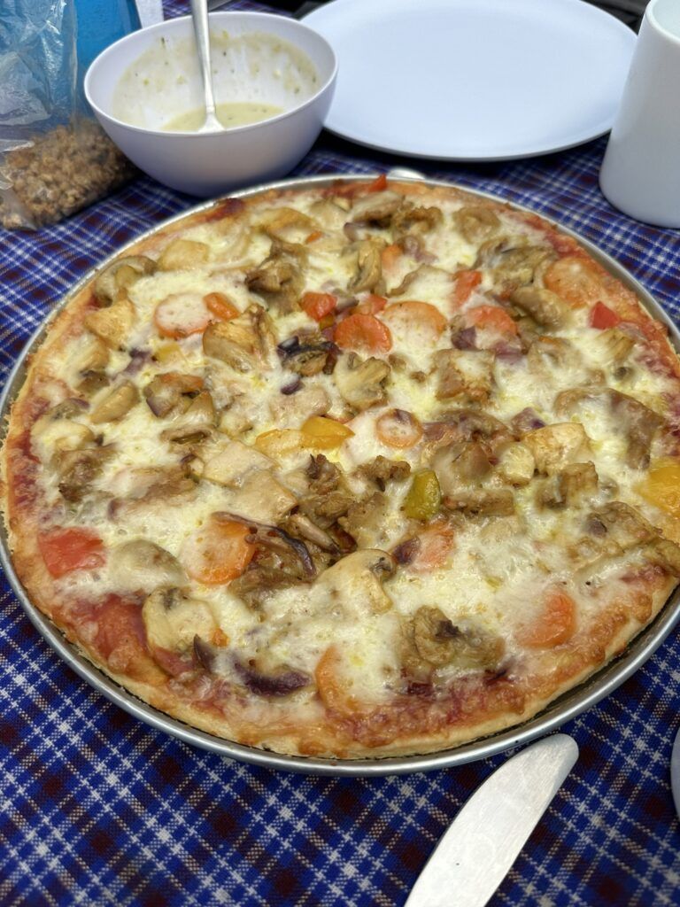 A pizza with mushrooms , tomatoes , onions and cheese is sitting on a table.