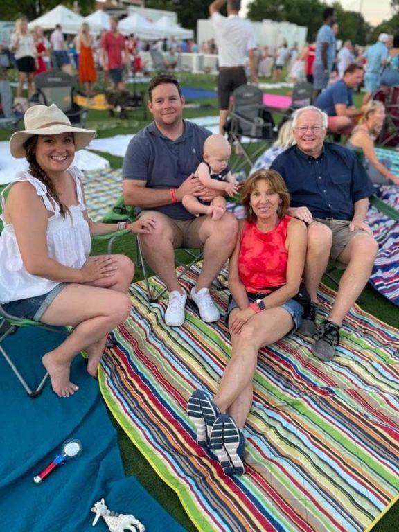 A group of people are sitting on a blanket on the grass.