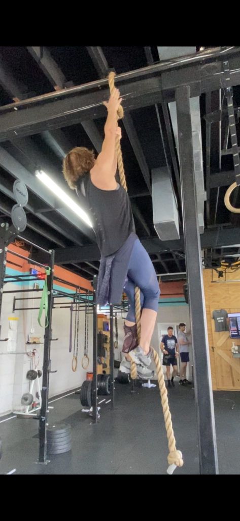 A woman is climbing a rope in a gym.