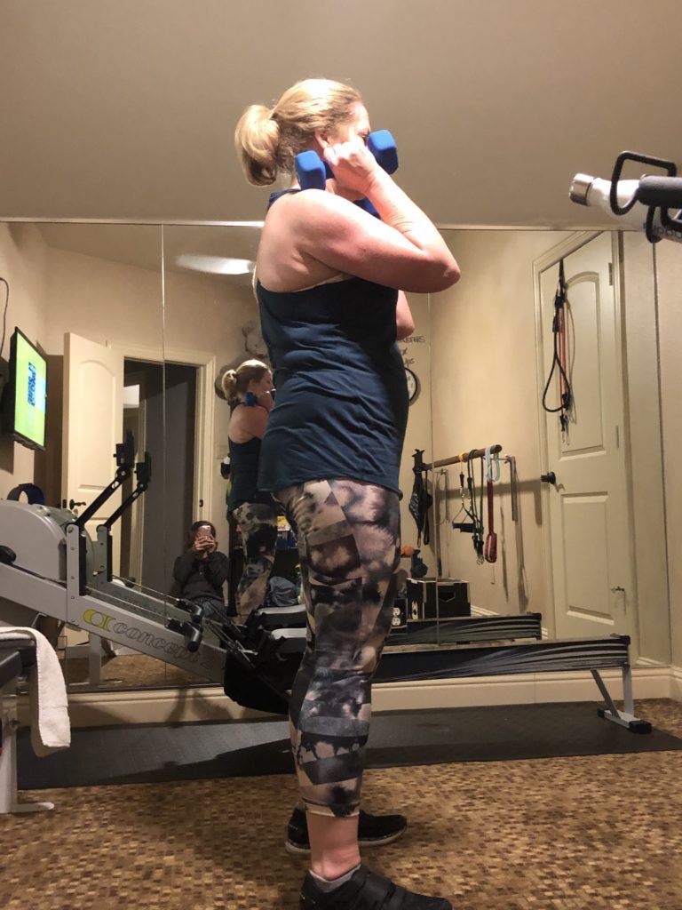 A woman is standing in front of a mirror in a gym holding a dumbbell.