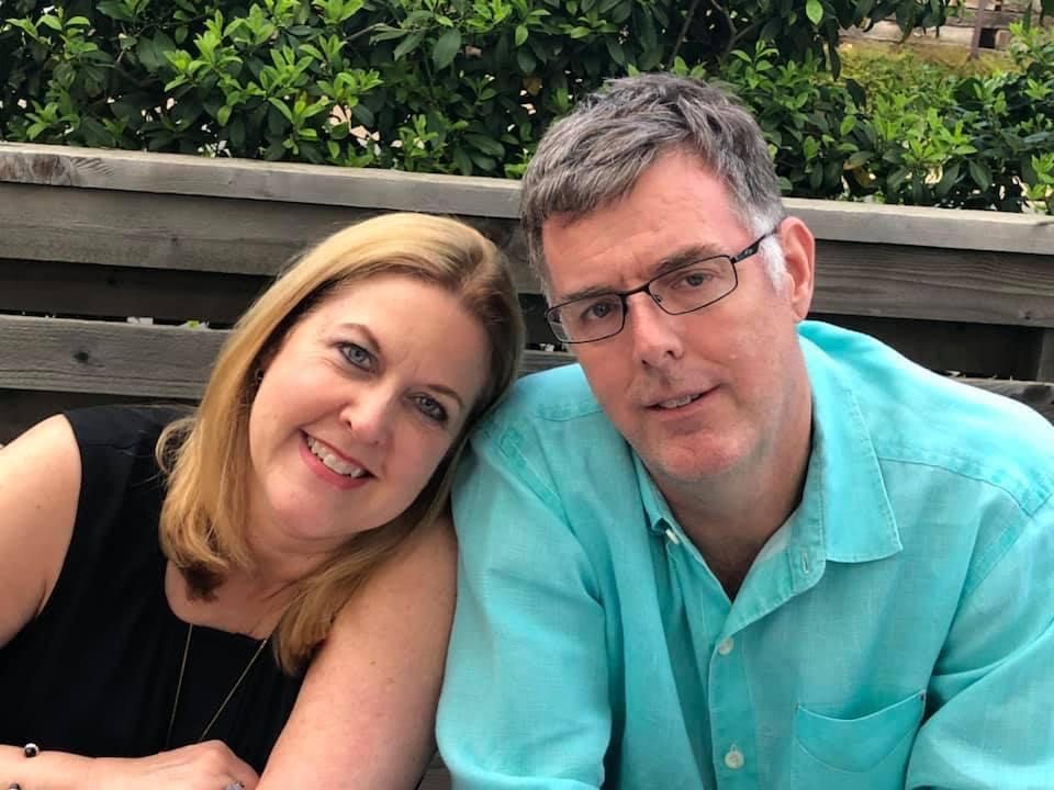 A man and a woman are posing for a picture while sitting on a bench.