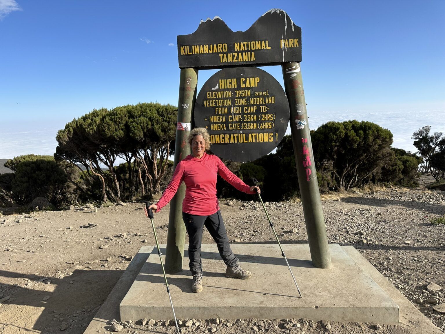 A woman stands in front of a sign that says kilimanjaro national park