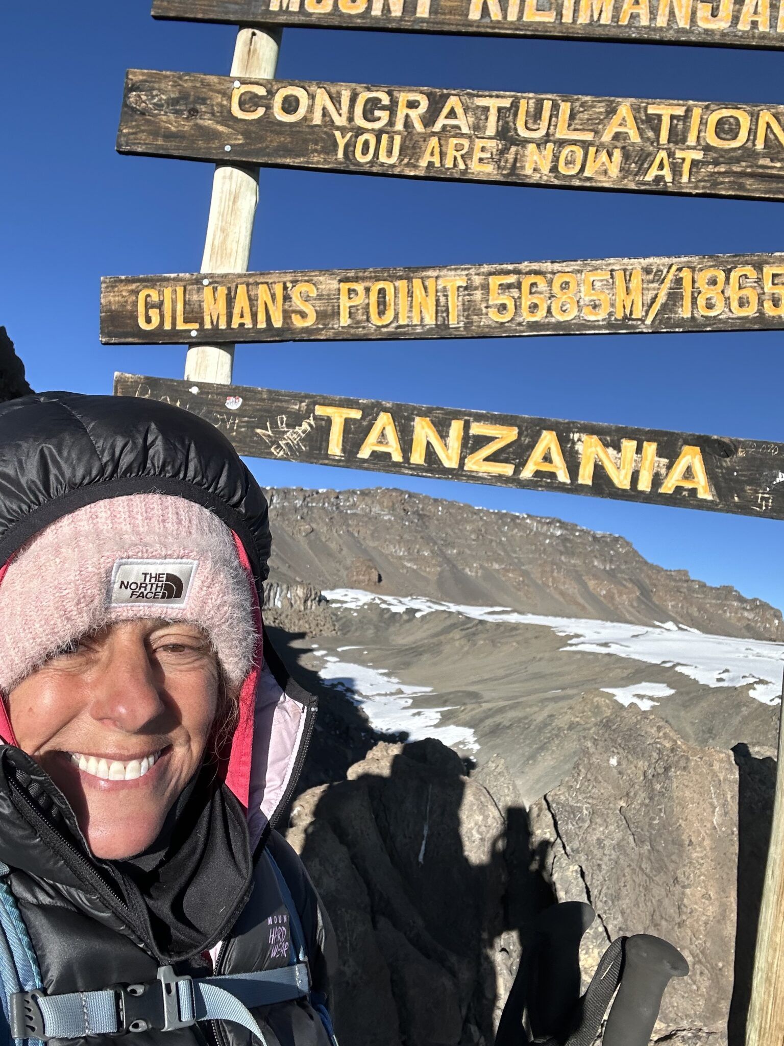 A woman is standing in front of a sign that says congratulations you are now at kilimanjaro.