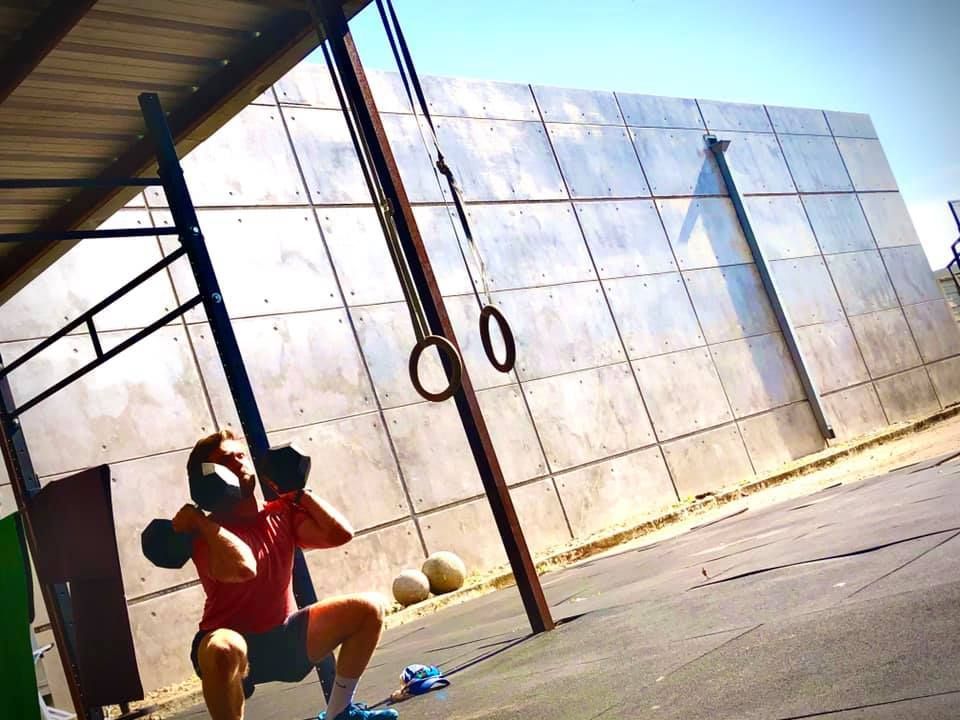 A man squatting down with a dumbbell in his hand