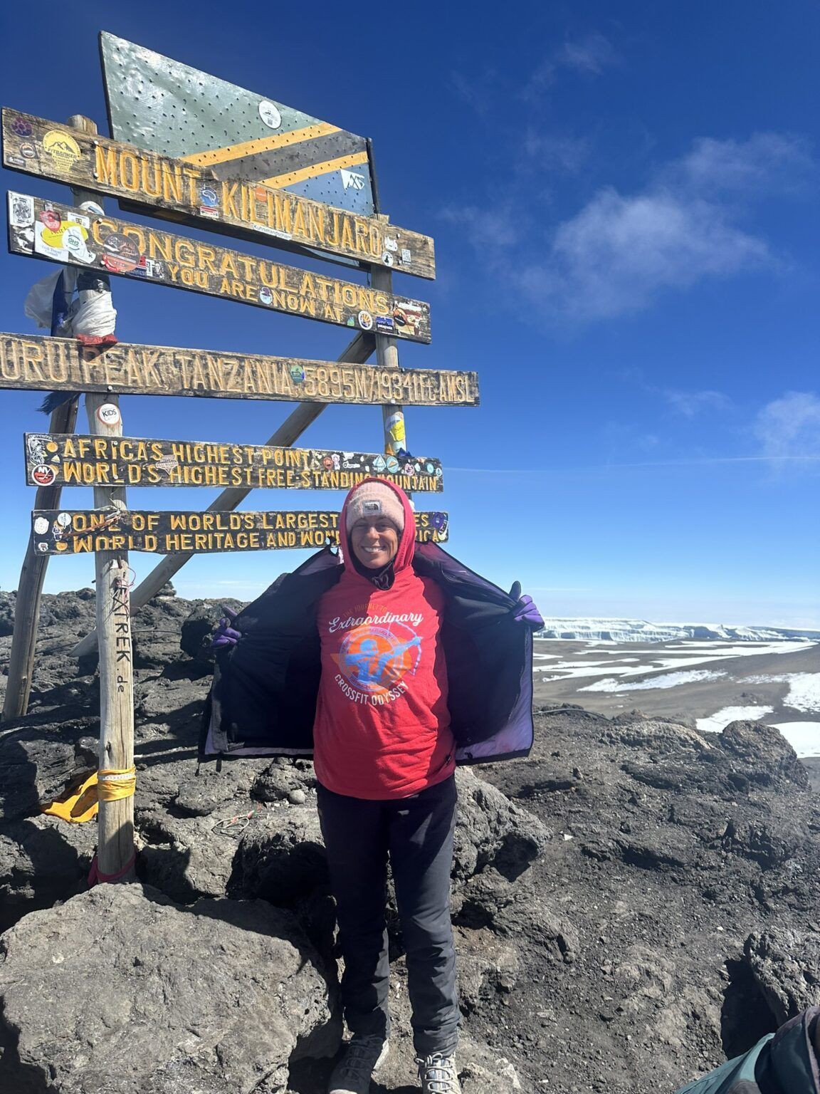 A woman in a red shirt is standing on top of a rocky mountain.