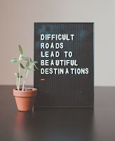 A sign that says `` difficult roads lead to beautiful destinations '' is sitting on a table next to a potted plant.