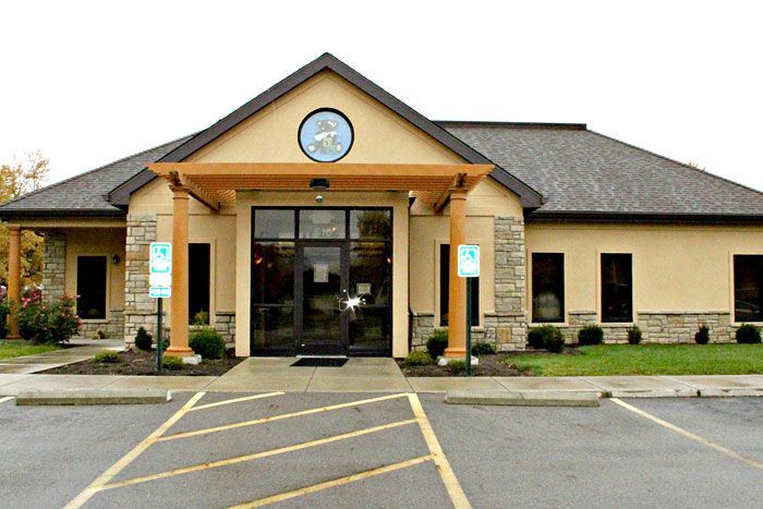 Exterior of a tan building with a brown roof and a wooden pergola over the entrance.