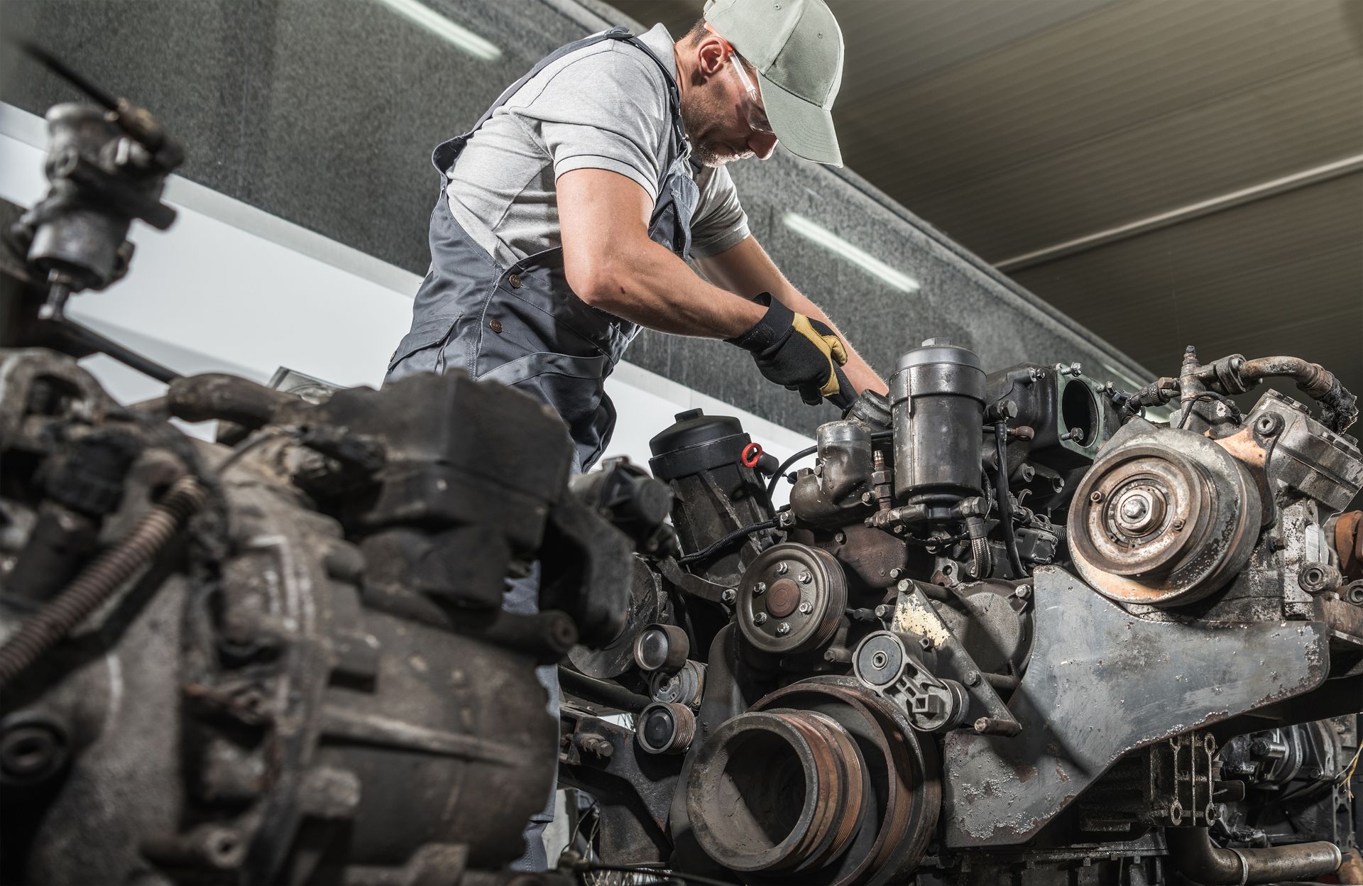 Mechanic inspecting a large engine in a workshop, surrounded by tools and machinery.