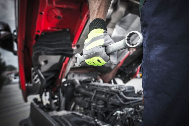 Mechanic using wrench on truck engine with red hood open.