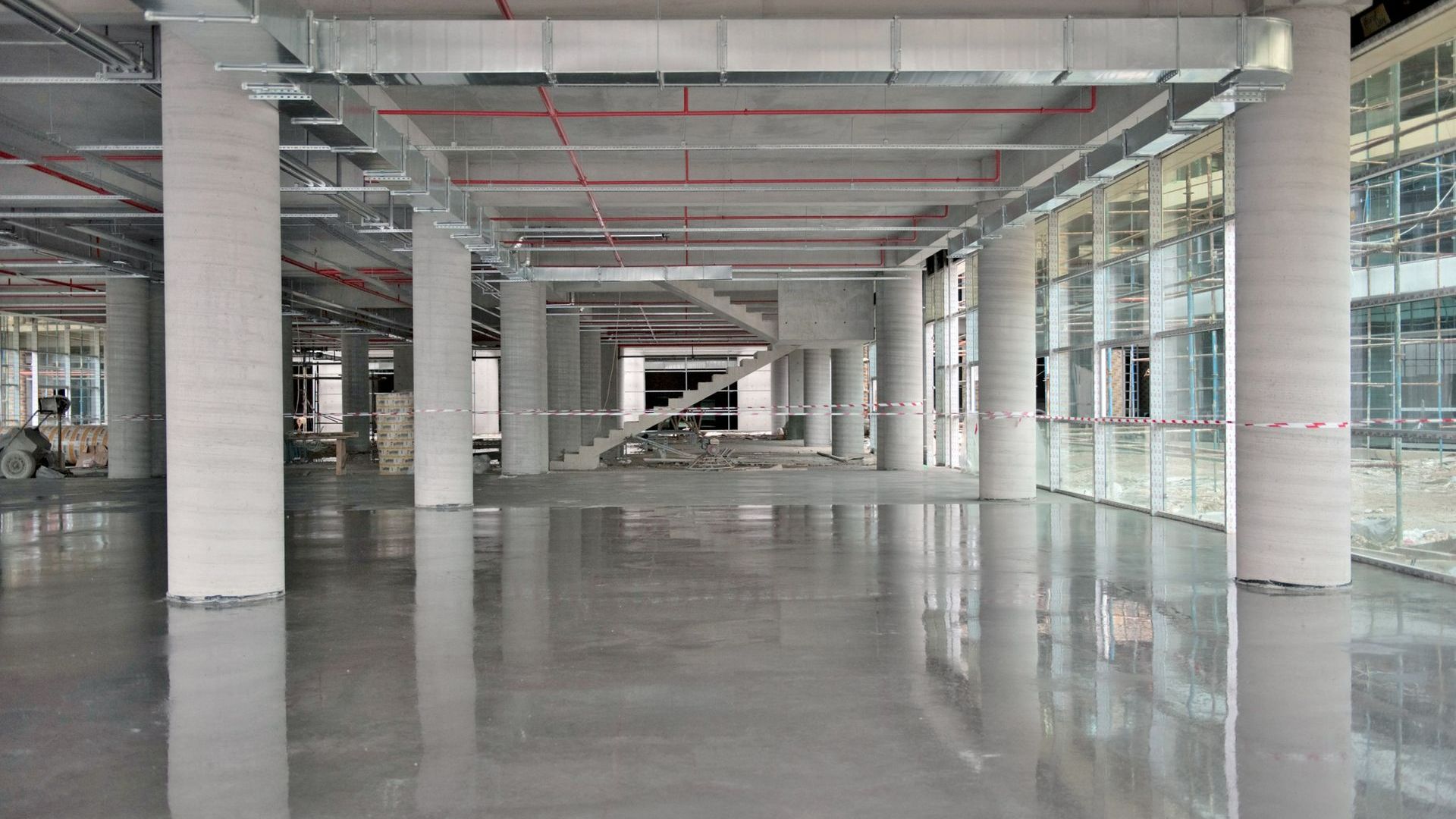 Empty, modern, interior space with concrete floor, columns, windows. Construction materials visible.
