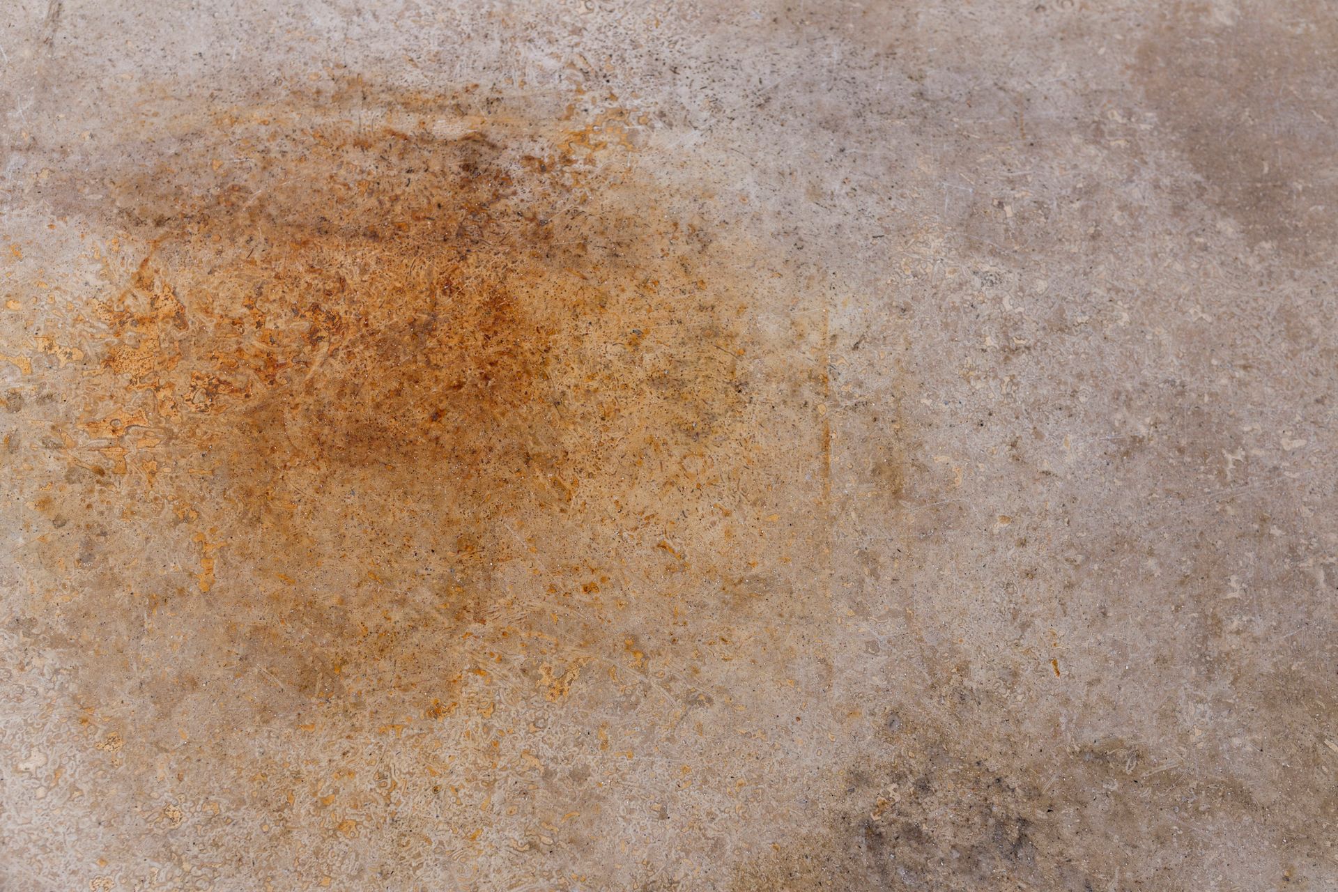 Close-up of a speckled, light-colored surface with a large, rusty brown stain in the center.