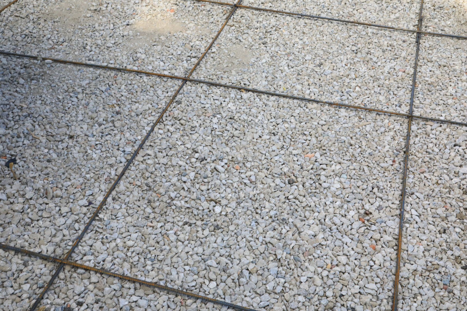 Gravel base with a grid of metal reinforcement bars, prepared for concrete pouring.