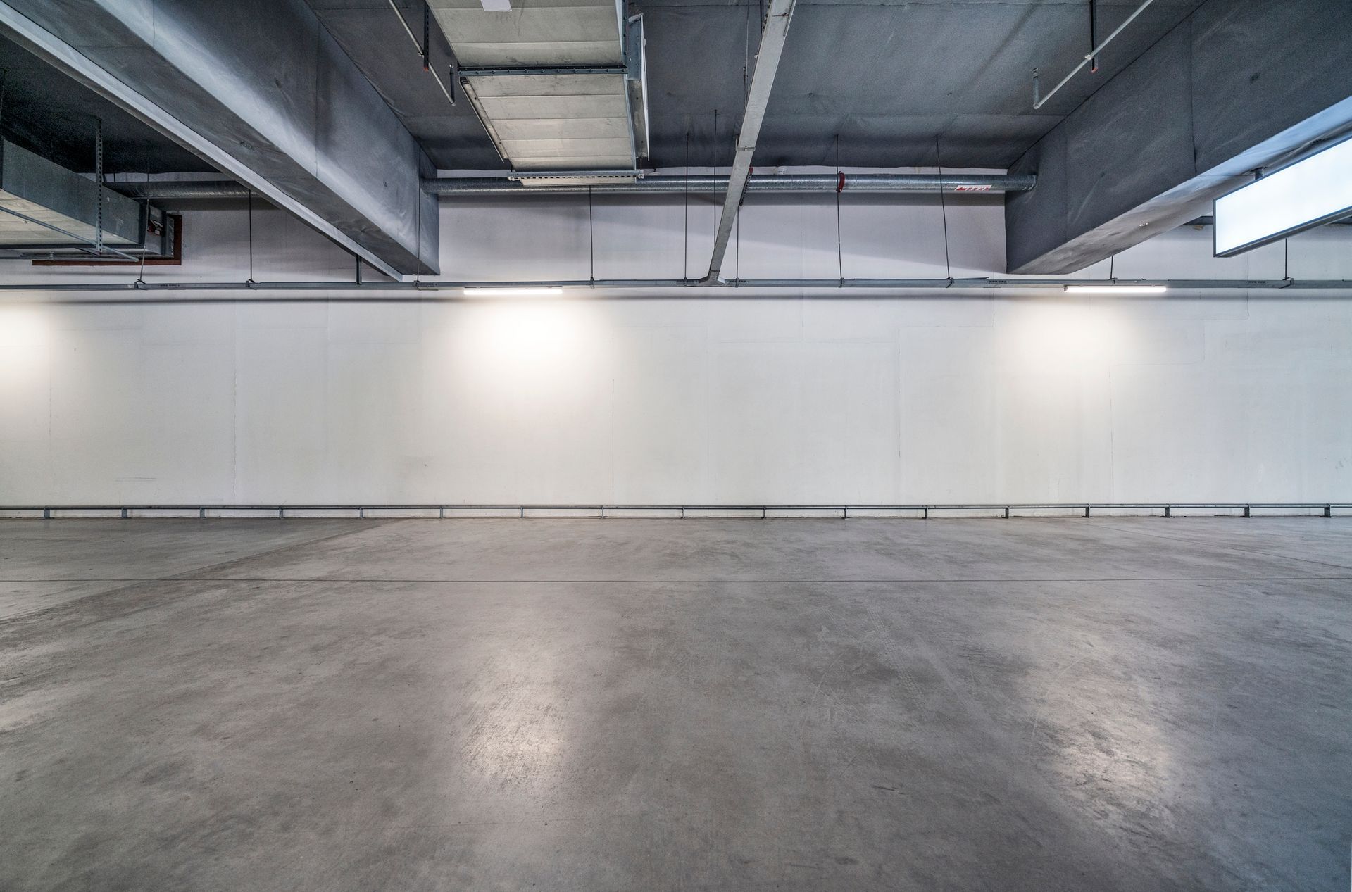Empty, modern room with concrete floor, white wall, and ceiling fixtures.
