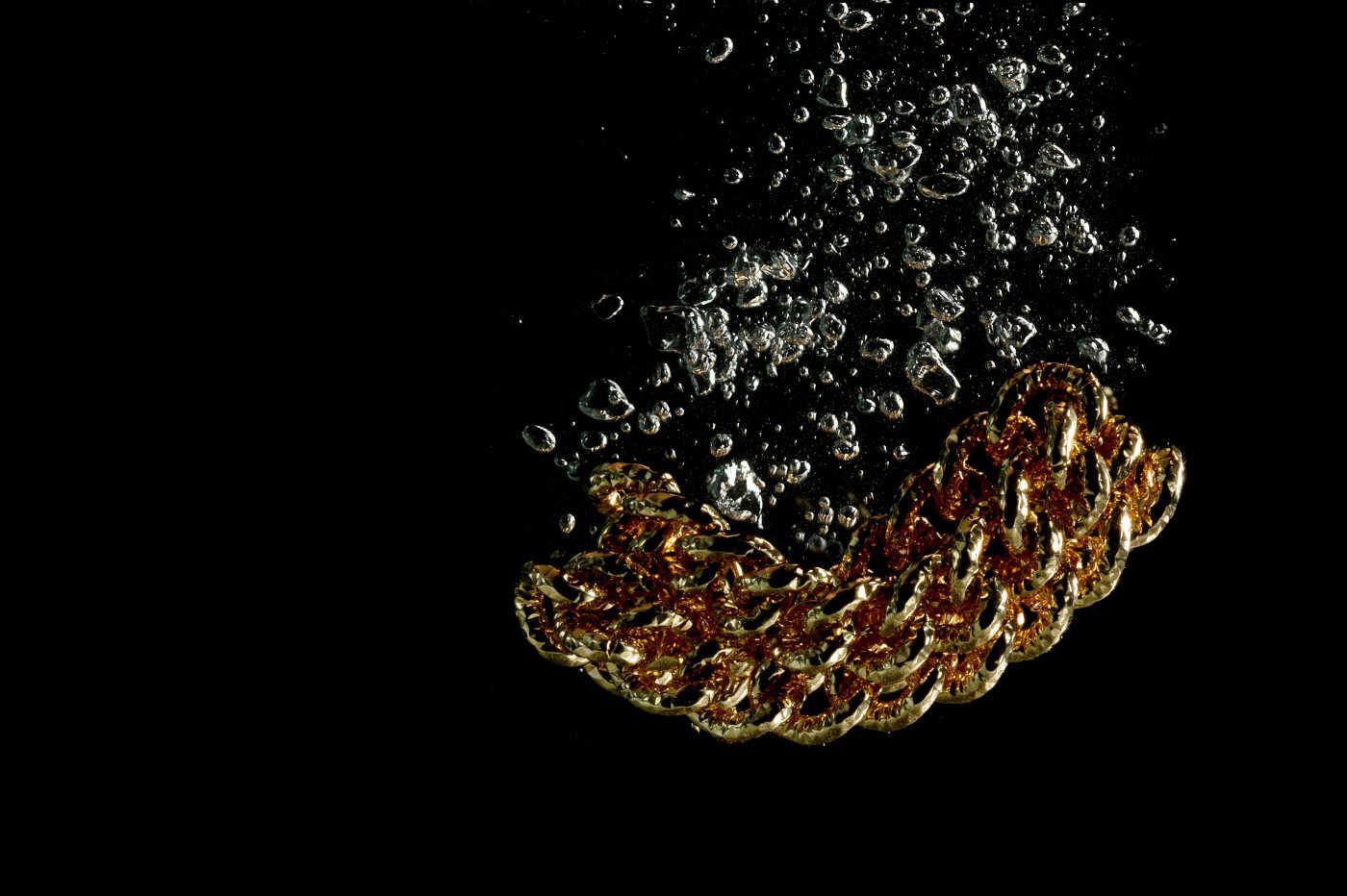 una catena d' oro sta cadendo nell'acqua su uno sfondo nero .