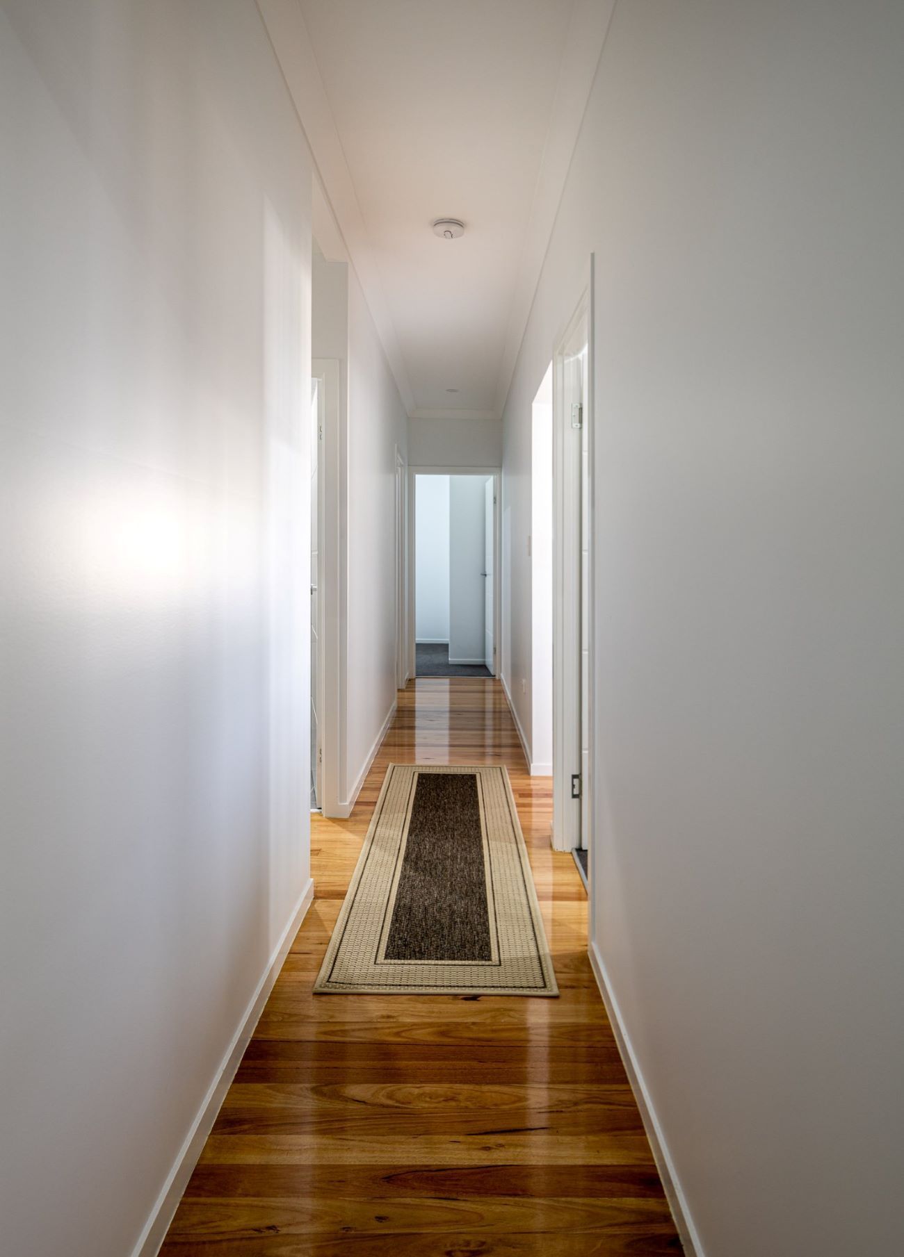 A Long Hallway With a Rug on the Floor and White Walls โ Wilkinson Homes in Annandale, QLD