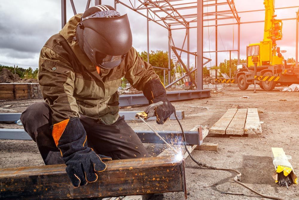 A Man Is Welding A Piece Of Metal On A Construction Site — NQES Industries in Ryan, QLD