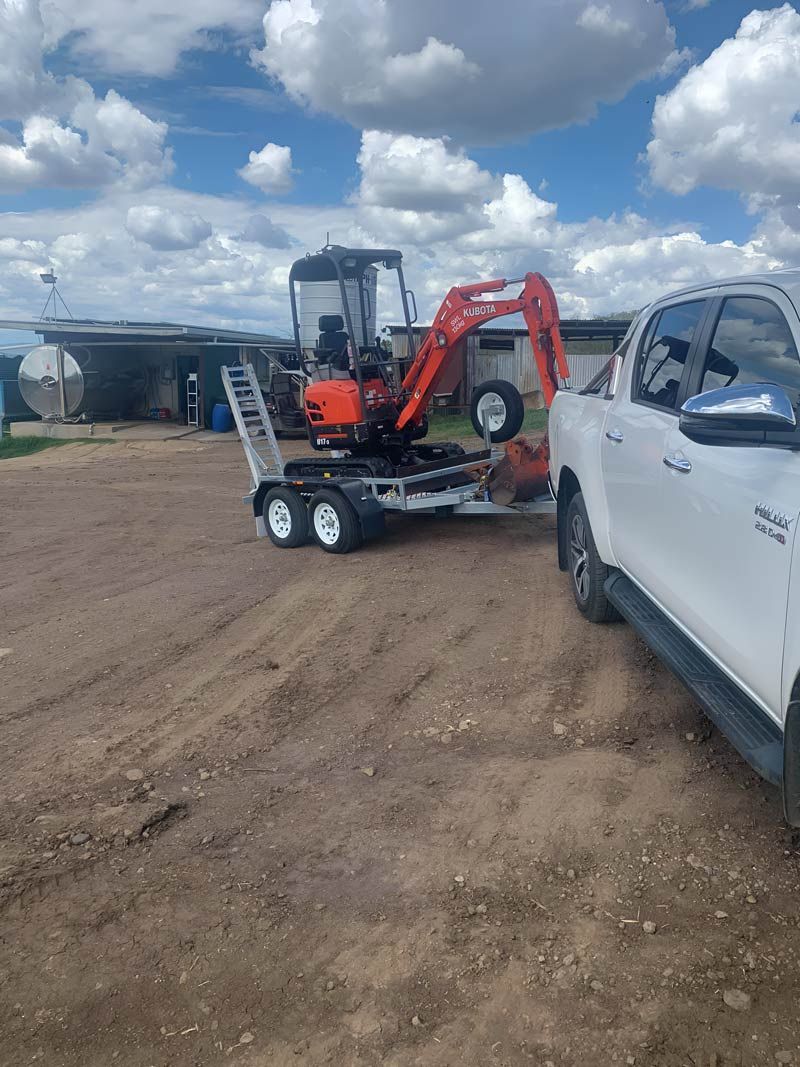 A White Truck Is Towing A Small Excavator On A Trailer — NQES Industries in Ryan, QLD