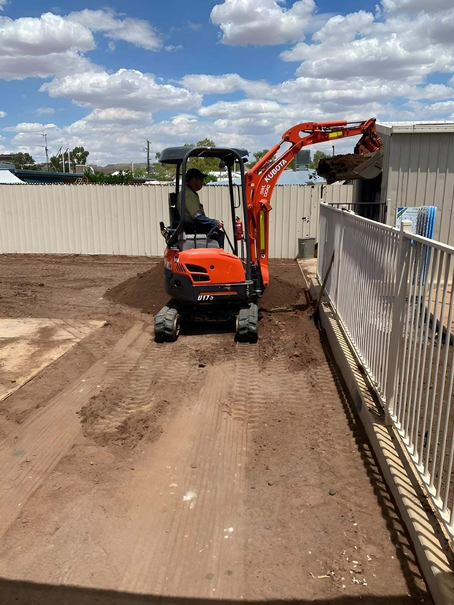 A Man Is Driving A Small Orange Excavator — NQES Industries in Ryan, QLD