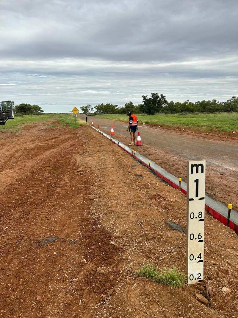 A Man Is Standing On The Side Of A Dirt Road Next To A Level Meter Level — NQES Industries in Ryan, QLD
