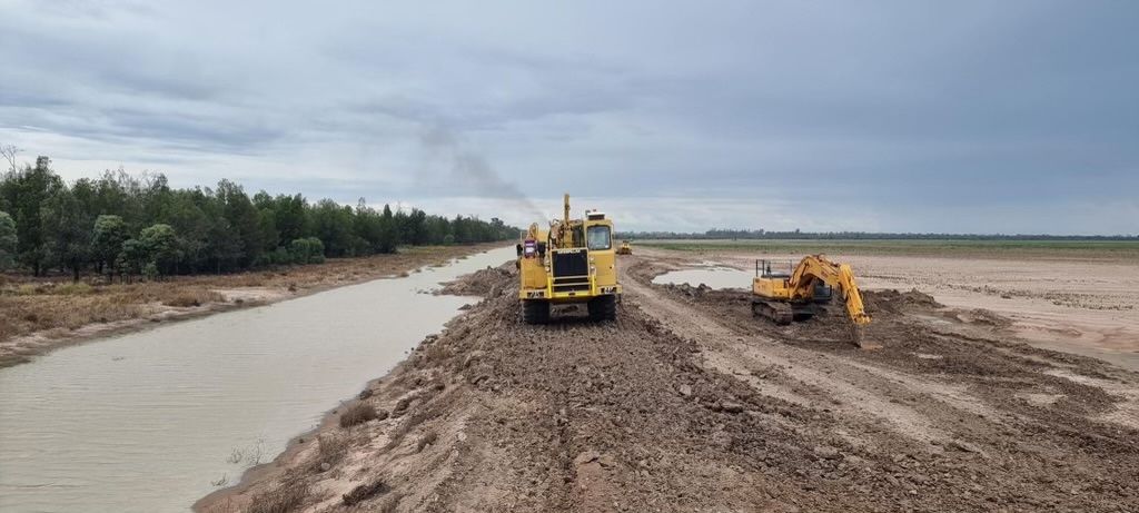 Two bulldozers are driving down a dirt road next to a river — NQES Industries in Ryan, QLD