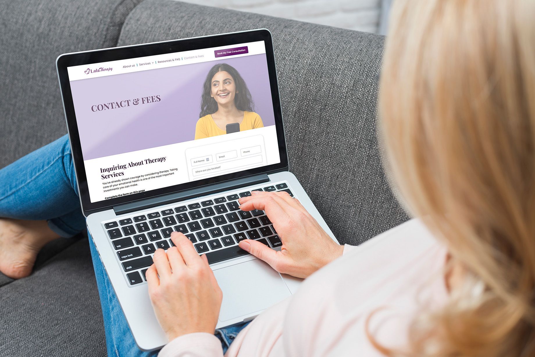 Person typing on a laptop showing a website with a smiling woman on a gray couch
