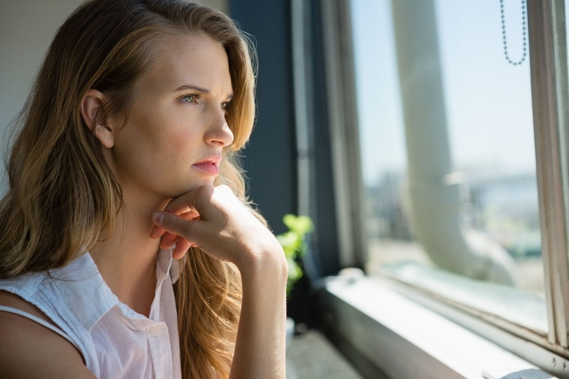 A woman looking out a window, reflecting, life transitions therapy for relocation in Fairfax, VA