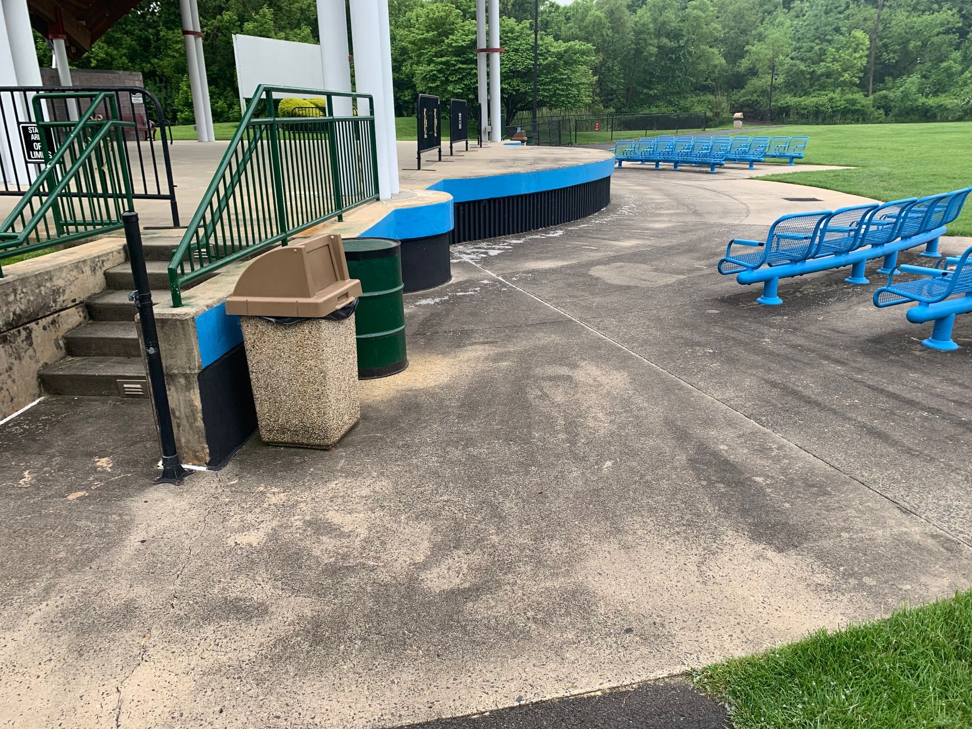 Outdoor amphitheater with blue seating and a stage with a trash can and green and black accents.