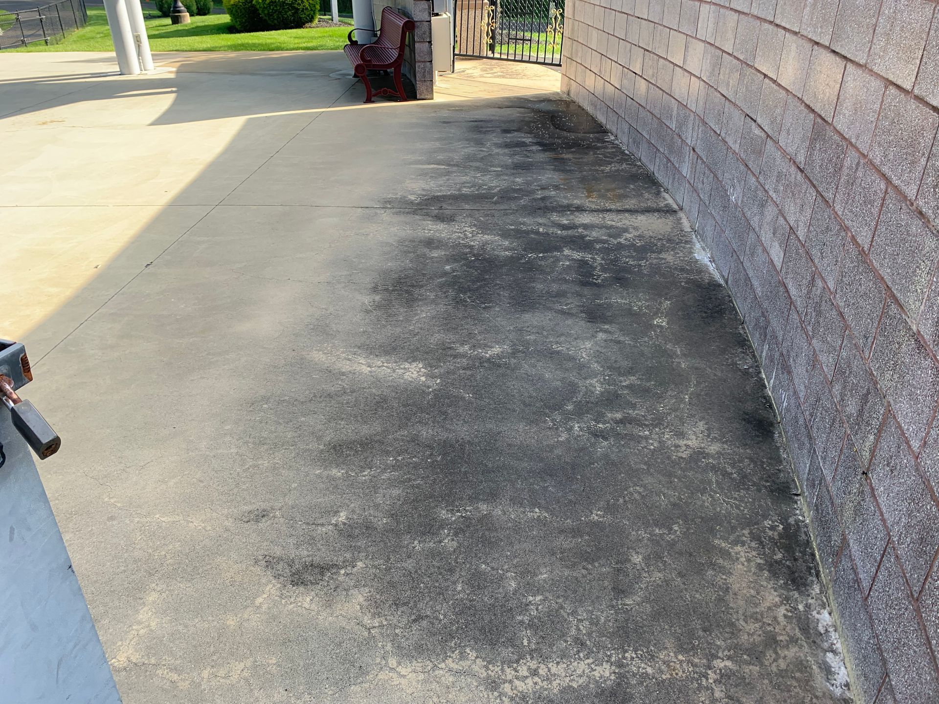 Concrete patio with dark stains next to a brick wall. Sunlight casts shadows.