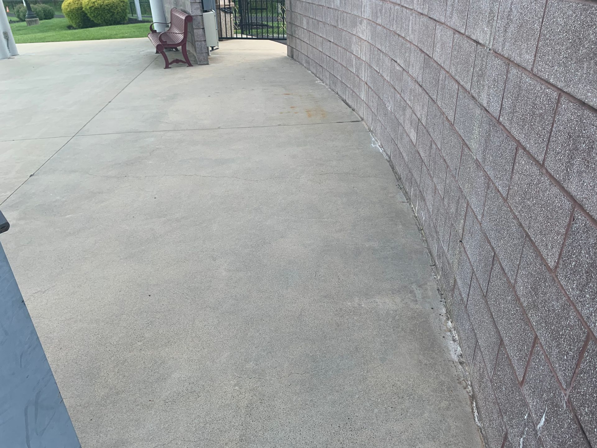 Concrete walkway beside a brick wall. A bench and gate are in the background.