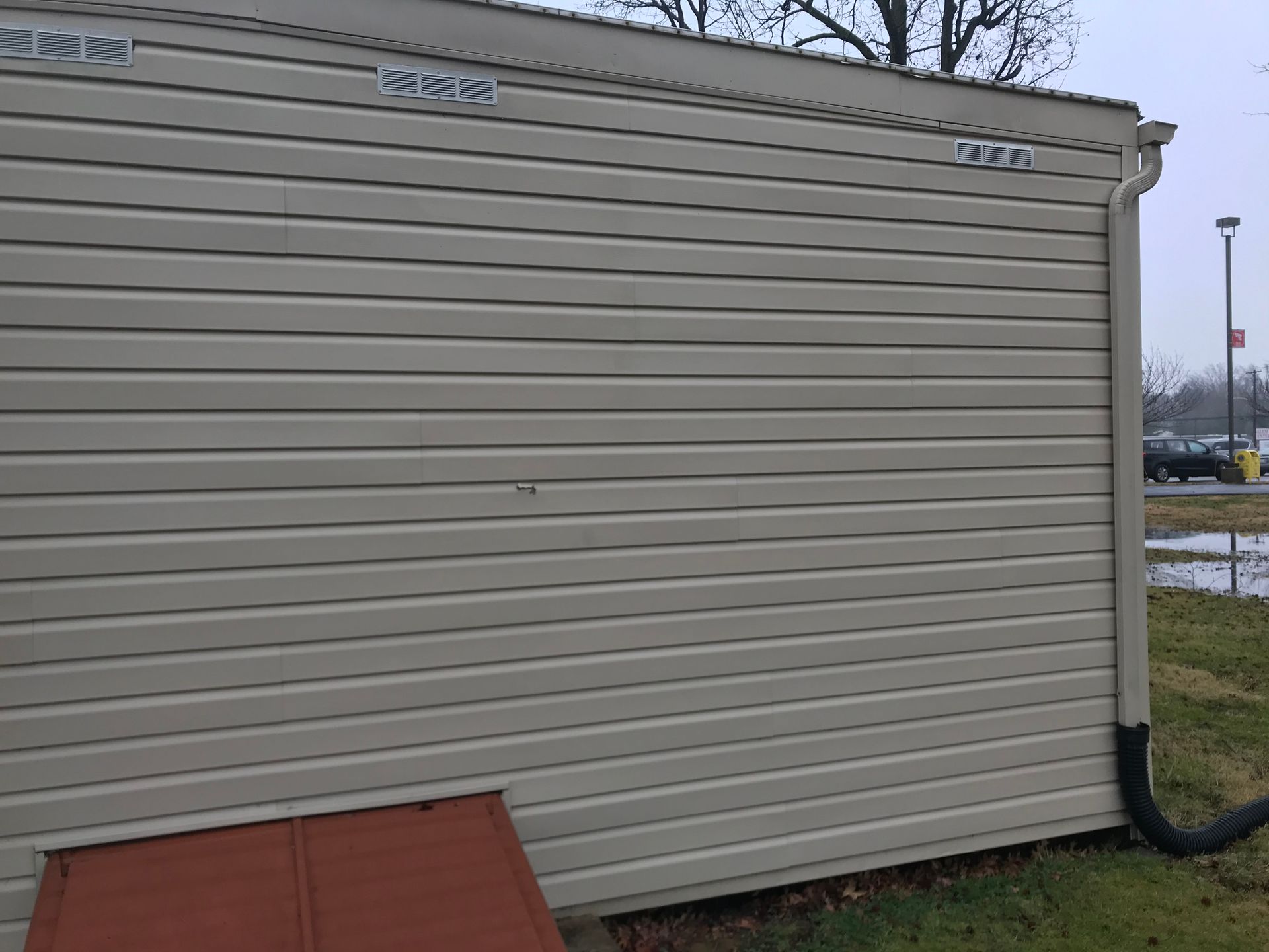Tan vinyl siding on a building, brown metal panel at bottom, black gutter.