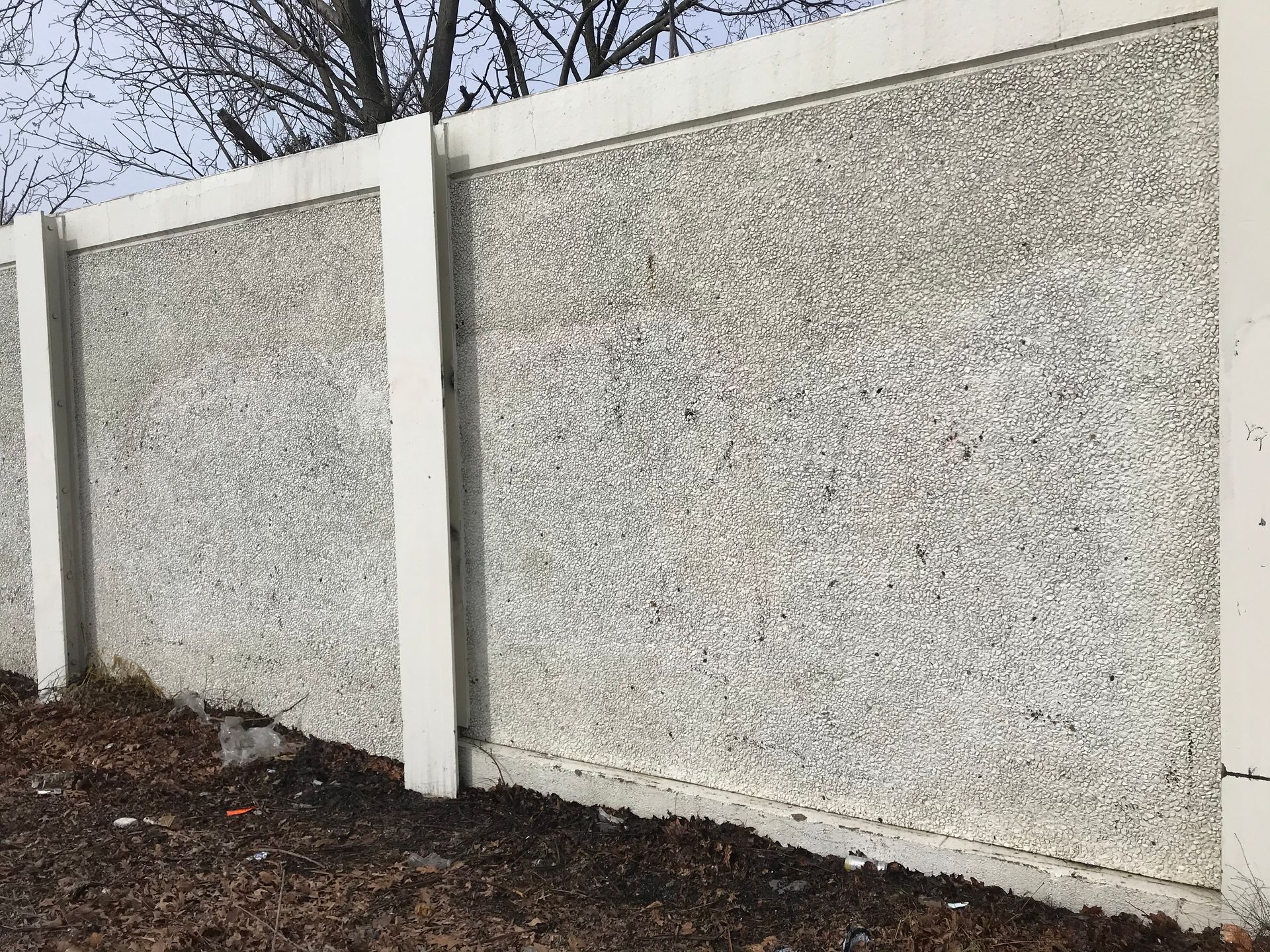 Gray concrete wall with white pillars, in outdoor setting.