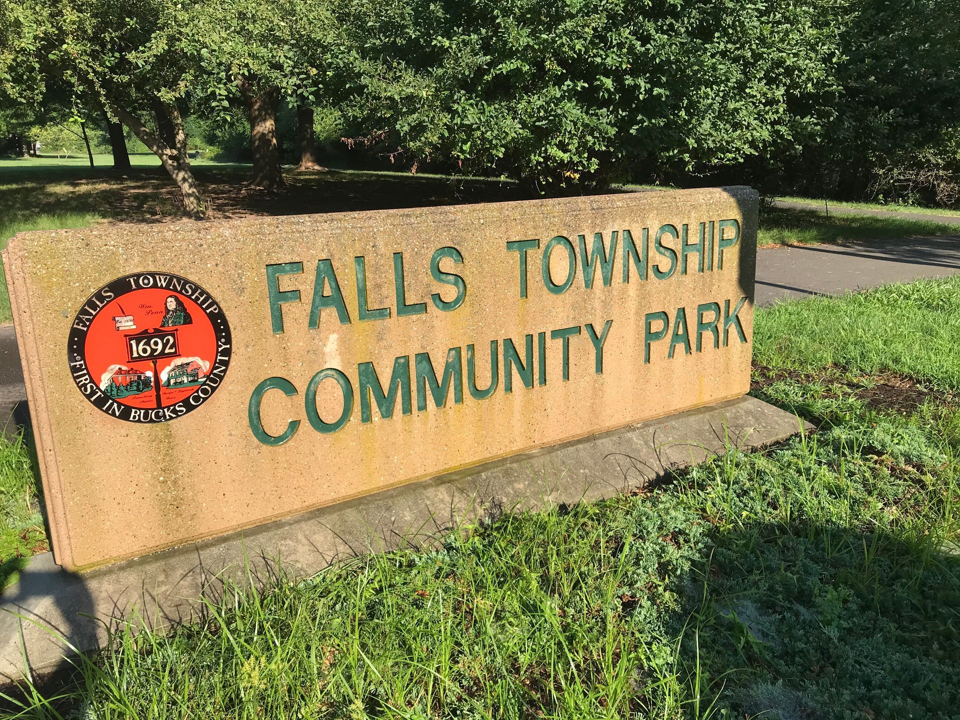 Sign for Falls Township Community Park, tan concrete with green lettering and logo; in a grassy park setting.