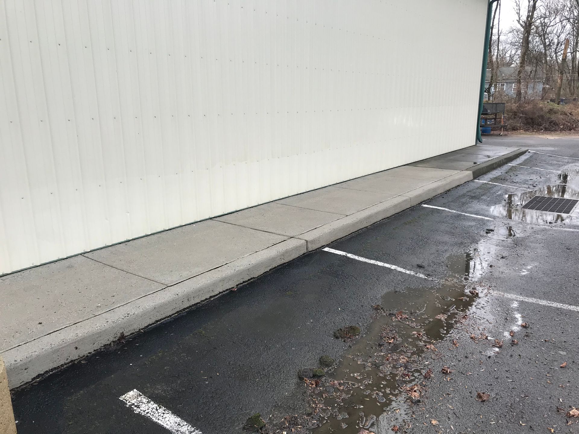 Concrete sidewalk next to a building with a white wall, adjacent to a parking lot.