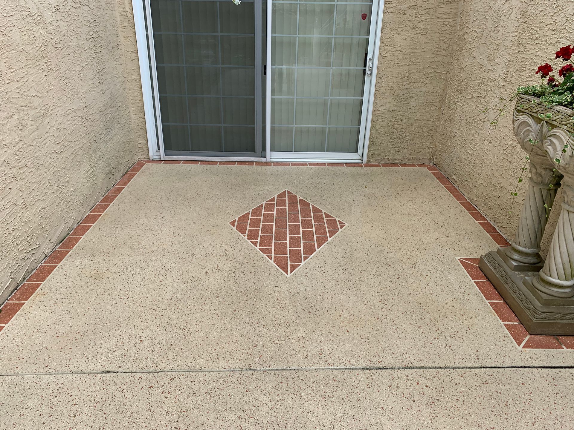 A concrete patio with a decorative brick pattern in front of a sliding glass door.