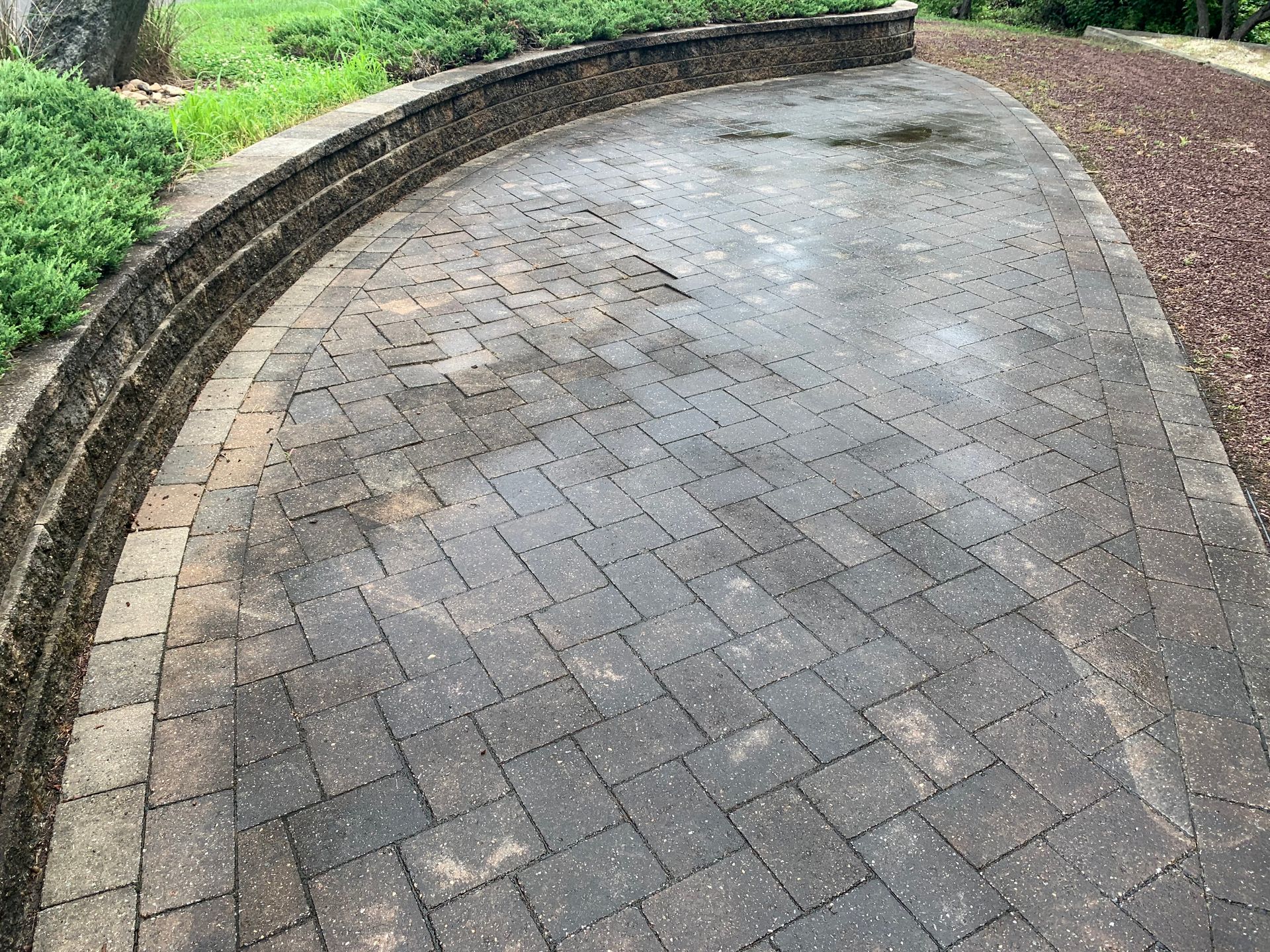Curved brick patio with low retaining wall and landscaping on either side.