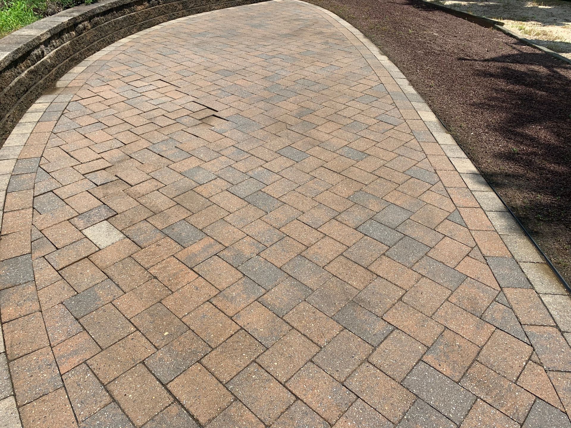 Brick pathway curving through a yard, bordered by dark mulch.