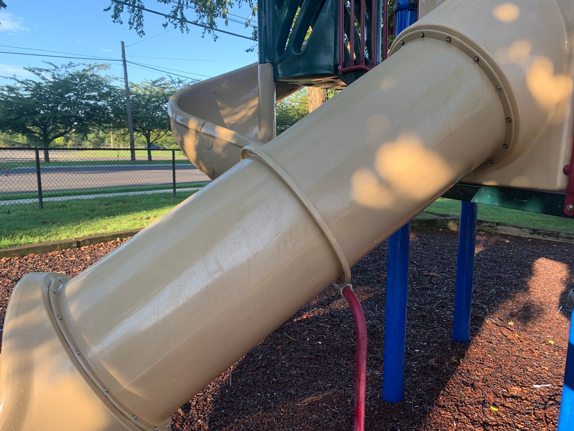 Tan playground slide with a curved tube, surrounded by wood chips and blue supports.