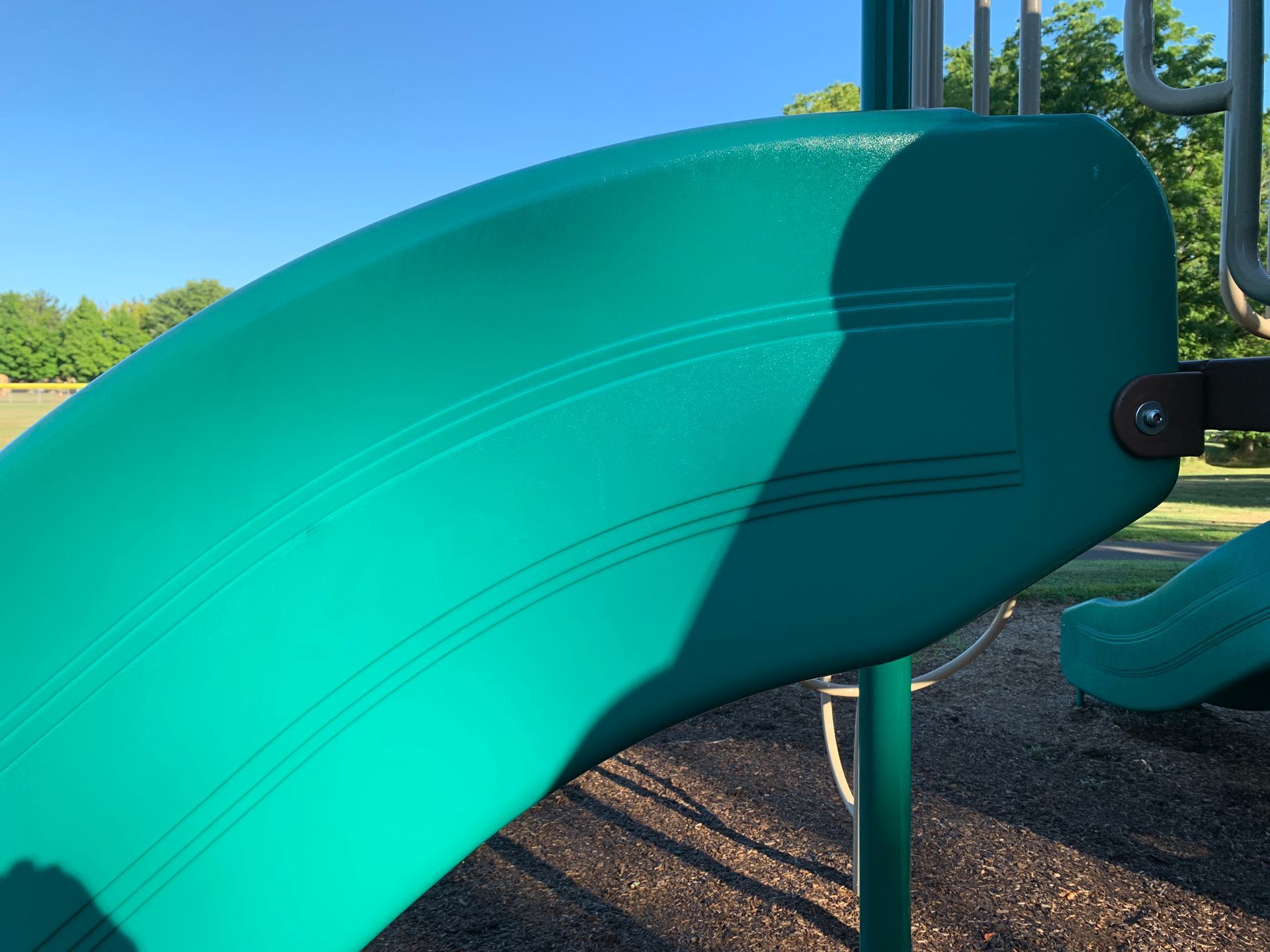 Green playground slide, curved, outdoors, sunny day.