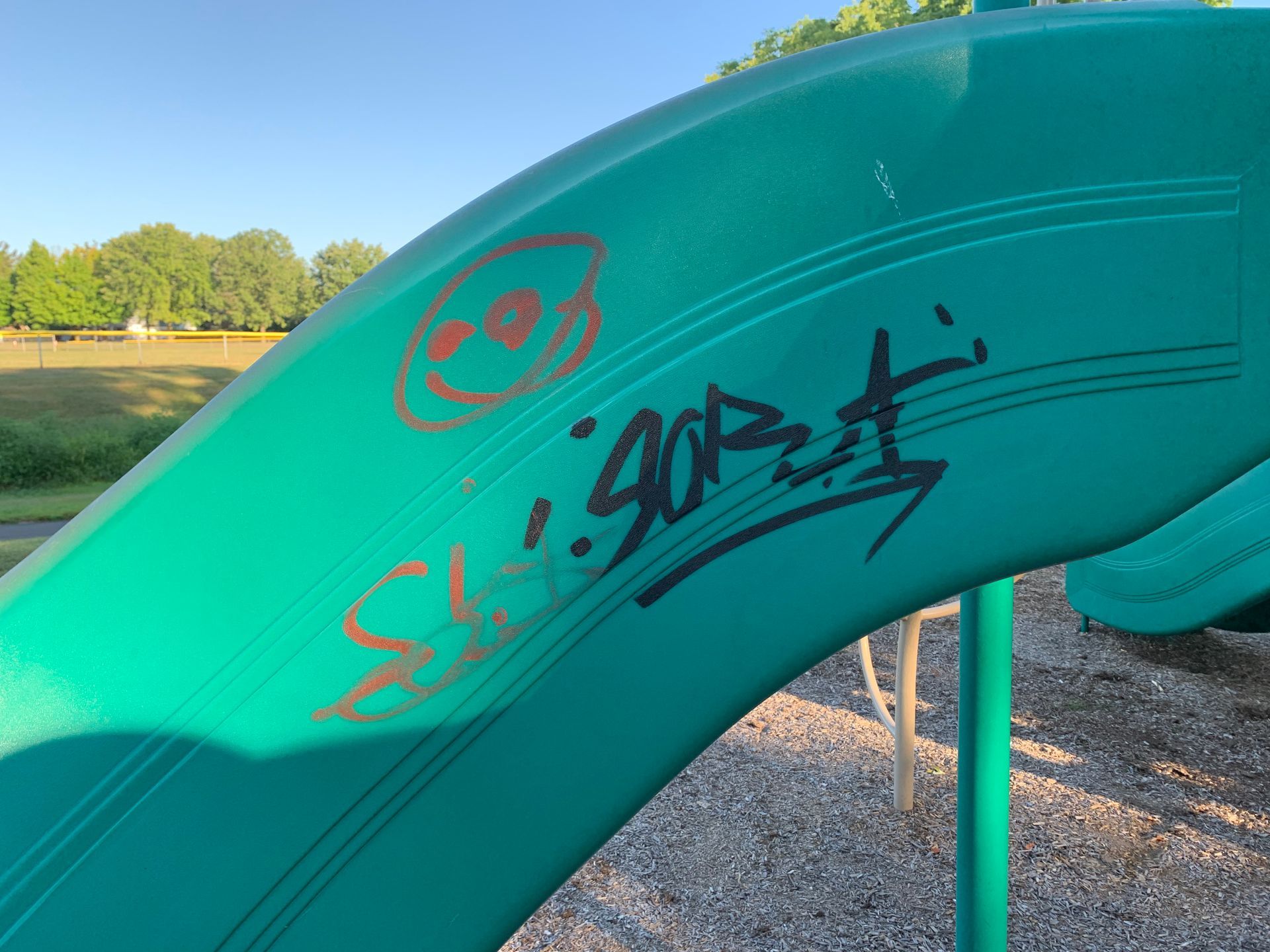 Green playground slide with graffiti in a park setting.