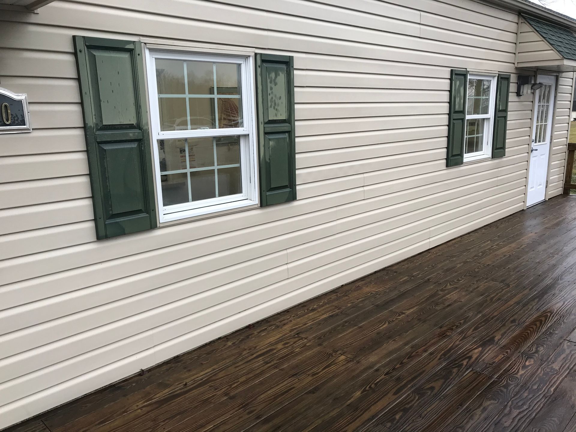 Tan-sided house with green shutters, white-framed windows, and a dark wooden deck.