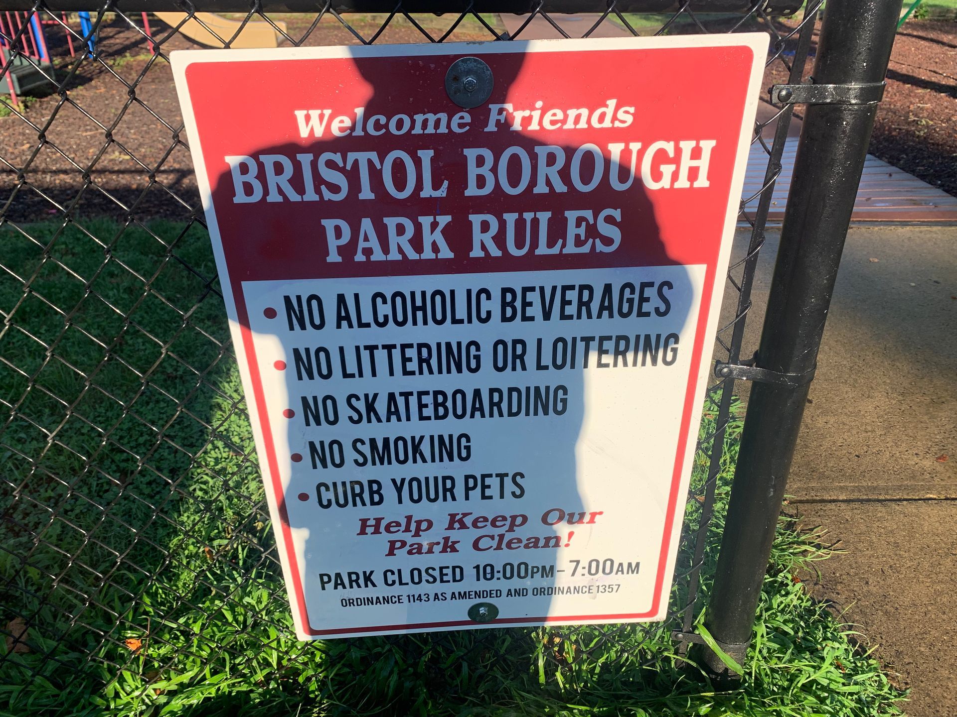 Sign with park rules in red and white on a fence, listing prohibitions: alcohol, littering, skateboarding, smoking, and pet control.